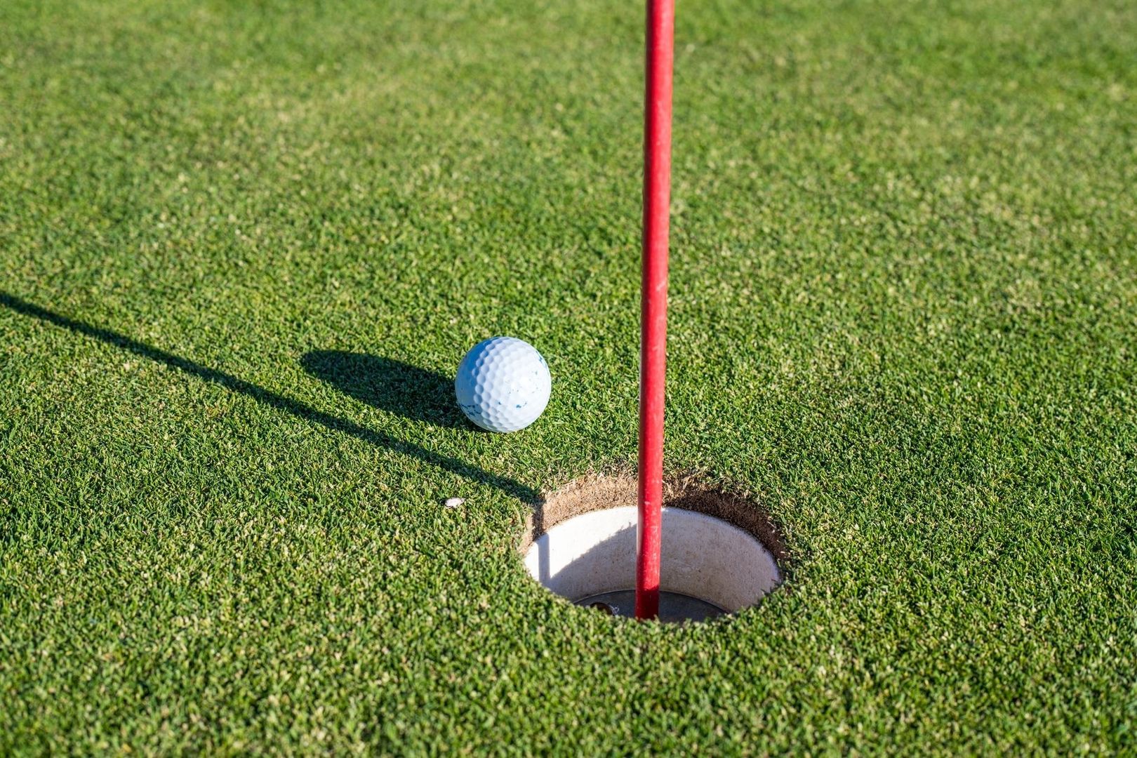 Golf ball resting beside the cup and red flagstick on a green