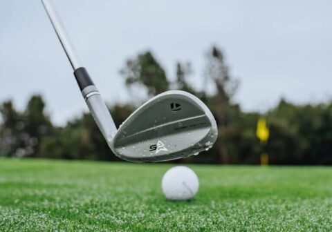 Wet iron club hovering just behind a golf ball on damp turf